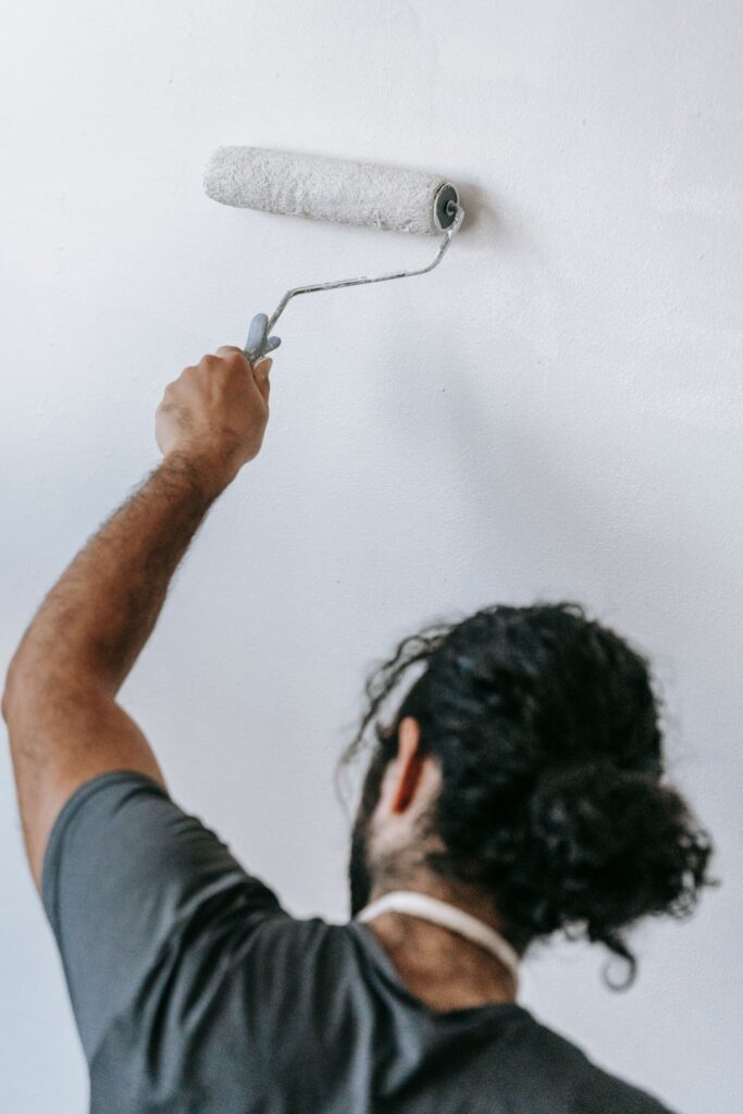 Homme peignant un mur intérieur blanc au rouleau dans un appartement.